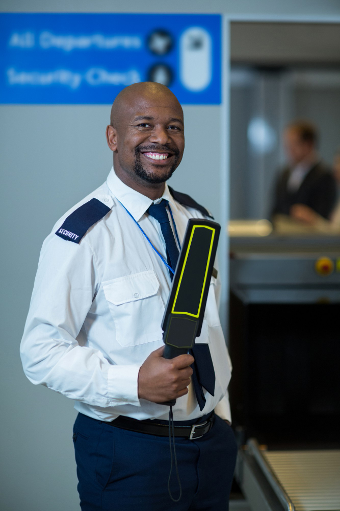 smiling-airport-security-officer-holding-metal-detector-in-airp p